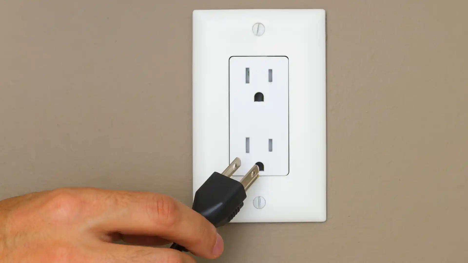 Hand plugging electrical cord into wall outlet showing proper electrical connection - Concord's Handyman Crew electrical repair services in Concord NC