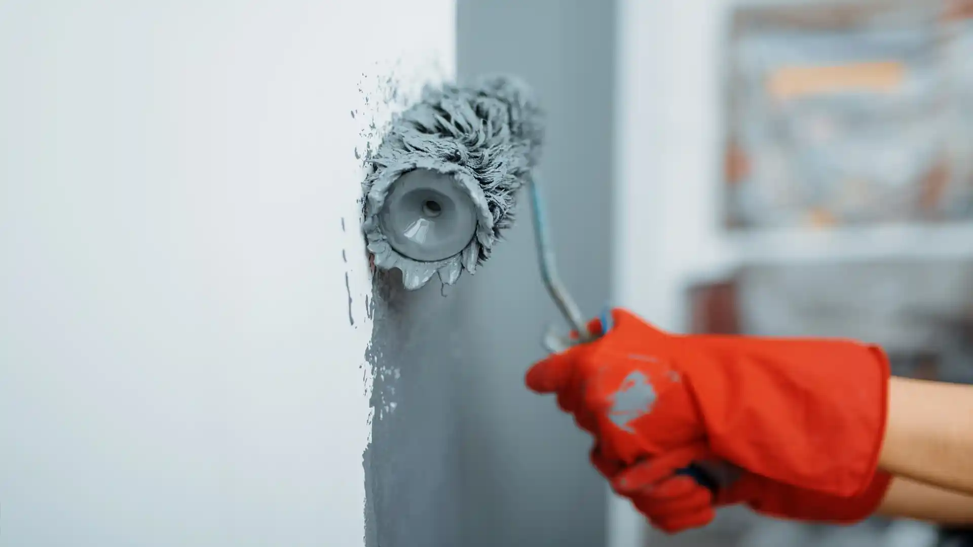 Professional painter using roller brush to apply fresh grey paint to interior wall during home renovation - Concord's Handyman Crew painting services in Concord NC