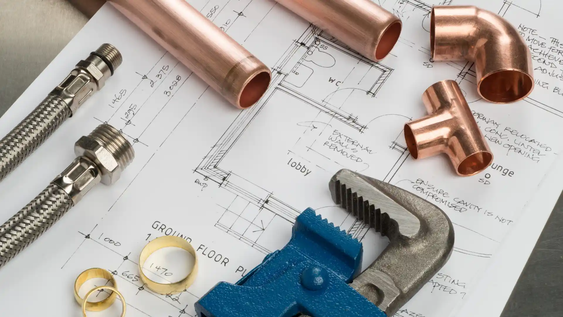 Professional plumbing tools including copper fittings, pipe wrenches and braided hoses laid out over detailed plumbing blueprints - Concord's Handyman Crew plumbing services in Concord NC