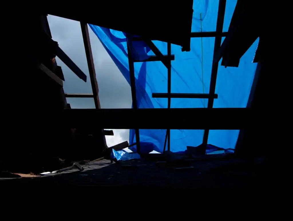 Damaged roof structure with blue tarps covering exposed rafters and debris from storm damage requiring emergency repair. Emergency roof repair in Concord NC showing Concord's Handyman Crew roofing services