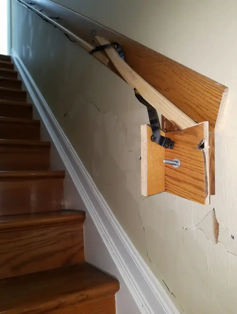 Wooden staircase handrail bracket pulled away from wall showing mounting hardware and drywall damage requiring repair. Stair handrail repair in Concord NC showing Concord's Handyman Crew carpentry services